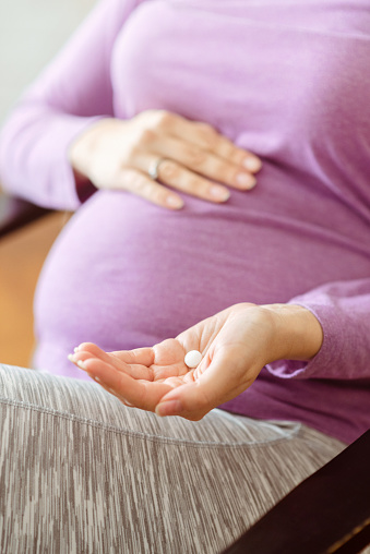 Close up of a pregnant woman holding a pill. prenatal vitamin, medication for healthy pregnancy.