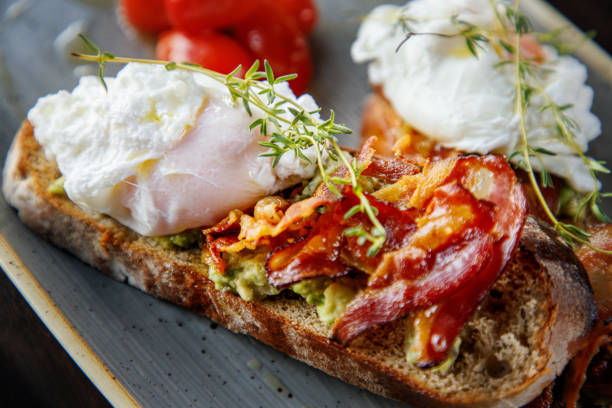 istock Close-up on poached egg and fried bacon with rosemary on bread slice with avocado 1388534054