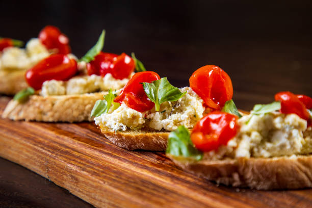 bruschetti con queso de cabra, tomate cherry y albahaca sobre tabla de madera - brushetta fotografías e imágenes de stock