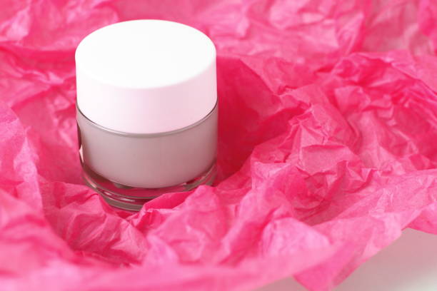 Light green cream, lotion in glass jar on pink paper bckground