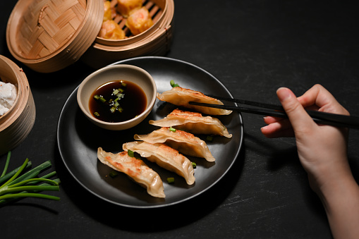 Female enjoy eating Asian fried gyoza or fried dumplings with chopsticks on a black restaurant table