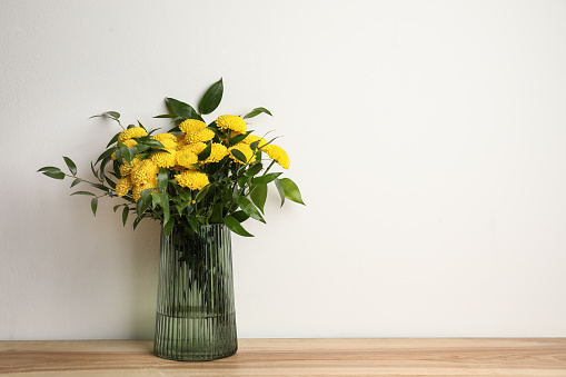 Bouquet of beautiful yellow flowers in glass vase on wooden table against white background. Space for text