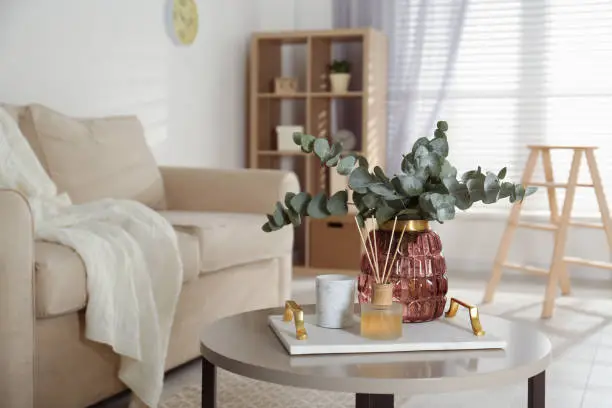 Bunch of eucalyptus branches and oil diffuser on table in living room. Interior design