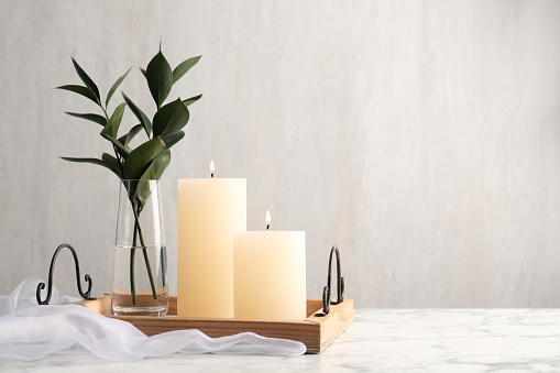 Beautiful burning candles and vase with green branches on white marble table. Space for text
