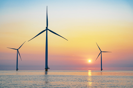 Wind turbines producing sustainable renewable energy in an offshore wind park in Flevoland, The Netehrlands, during sunset. Drone point of view.