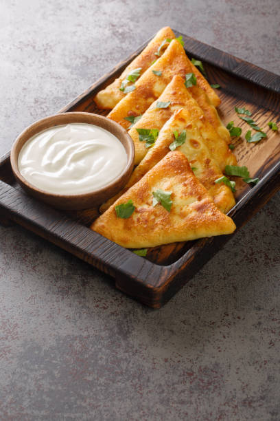 istock Triangular fried pancakes with meat served with sour cream close up on a wooden tray. Vertical 1388540091