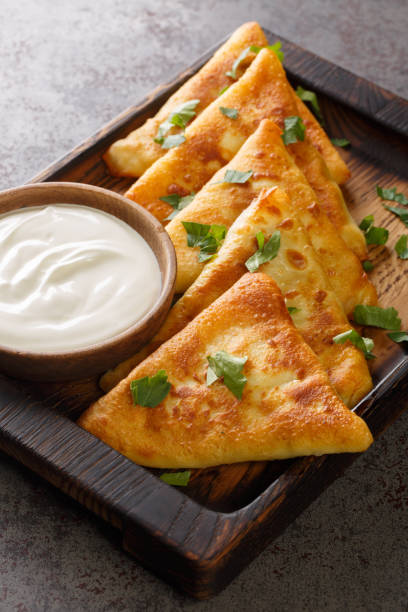 istock Ukrainian triangular fried pancakes benderyki served with sour cream close up on a wooden tray. Vertical 1388540111
