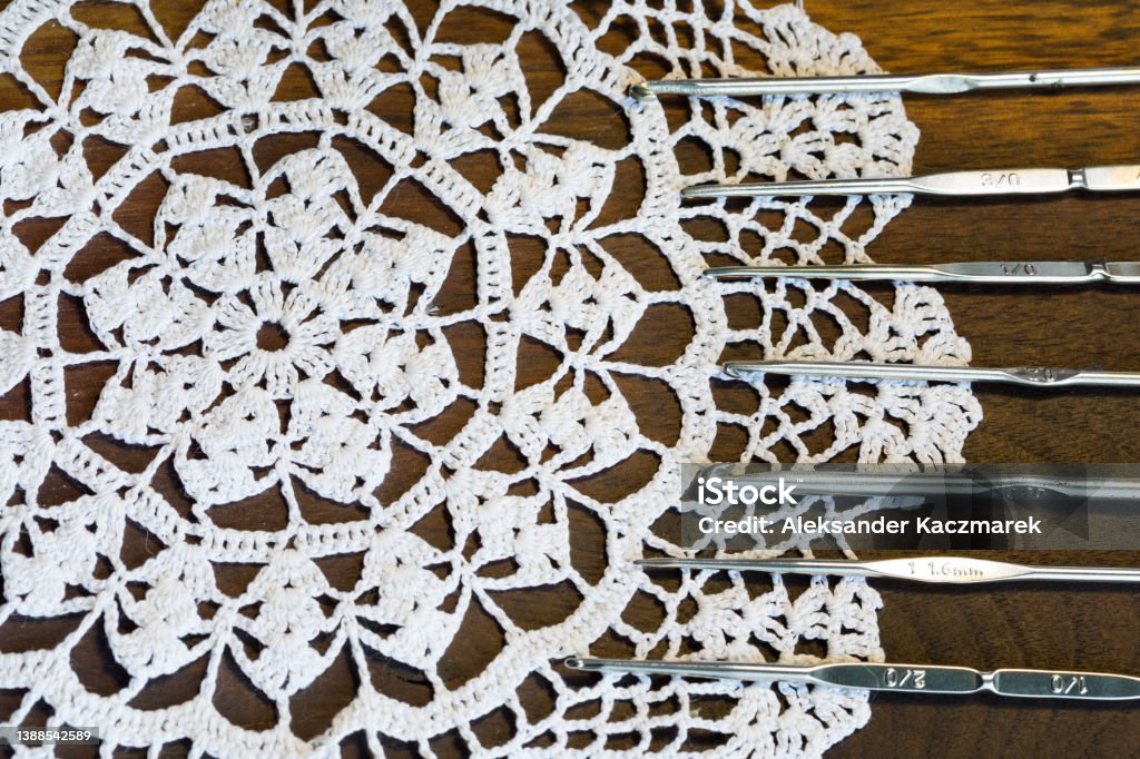 Set of crochet hooks lying on a lace doily Top view of set of metal crochet hooks lying on a white lace doily Art Stock Photo
