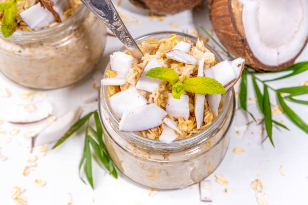 Breakfast overnight oatmeal oats with coconut milk and fresh coconut pieces. Diet healthy food, vegan diet. On light background with fresh coconuts and palm leaves, copy space