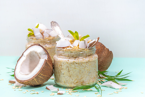 Breakfast overnight oatmeal oats with coconut milk and fresh coconut pieces. Diet healthy food, vegan diet. On light background with fresh coconuts and palm leaves, copy space