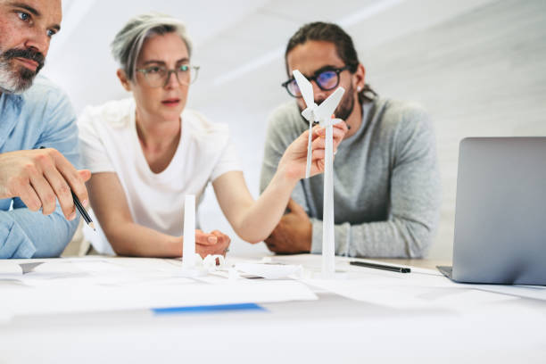 Innovative businesspeople working on a wind turbine project Innovative businesspeople working with 3D wind turbine models in a modern office. Group of creative design professionals having a discussion while working on a renewable energy project. industrial designer stock pictures, royalty-free photos & images