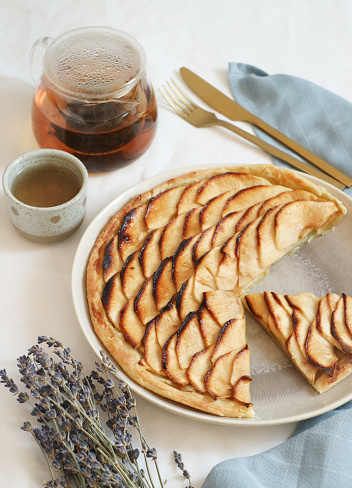 A plate of classic traditional French apple tart fine(tarte fine aux pommes) caramelized with brown sugar. With a cutting pieces &Tea pot and cup in background.This tart made with butter puff pastry