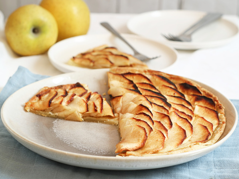 Plate of a classic traditional French apple tart fine(tarte fine aux pommes) caramelized with brown sugar in a plate. With its fruit and fork in background. This tart made with butter puff pastry