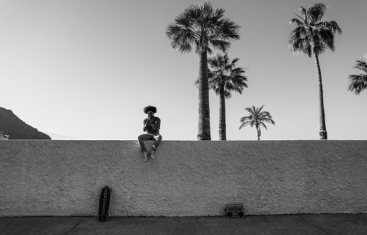 African man listening music with vintage boombox stereo outdoor while using mobile phone - Focus on face - Black and white edition