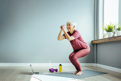 Full length view of an active woman in her 60s working out and doing some squats at home