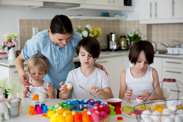 Three children, sibling brothers, painting easter eggs for decoration, mom helping them