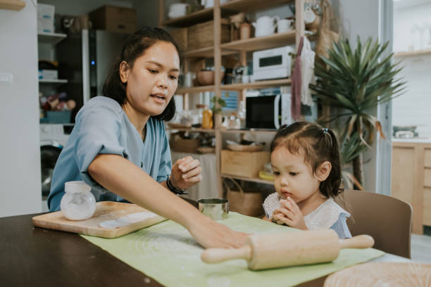 Homeschooling, Feeling excited to joy helping mom preparing food. Cute Thai girl sitting with her mom waiting for helping her mom making dumpling sheet for lunch. asian nanny stock pictures, royalty-free photos & images