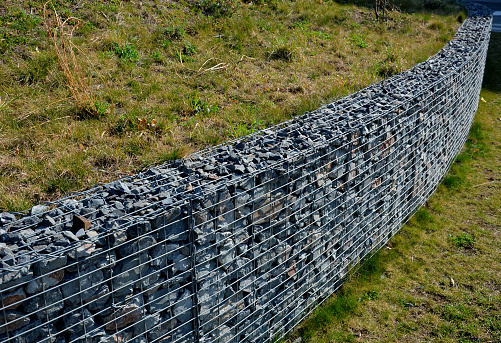 construction of a gabion retaining wall, as part of the house fencing. workers put geotextiles and on it wire baskets which consists of granite stones. demanding manual work, stabilizer, stability, stacked, geotextile
