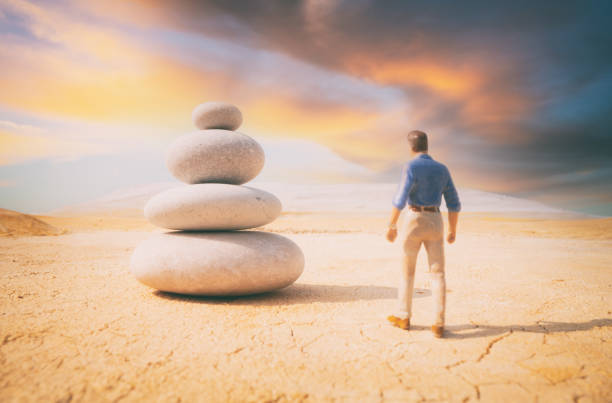 A man stands alone in a vast open desert. In front of him is a large stone cairn. Who is he, who built the cairn, and what does it all mean..? Who knows. \n\nScale model photography.