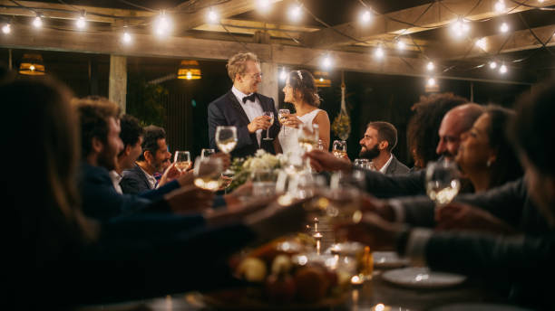 아름다운 신부와 신랑은 저녁 리셉션 파티에서 결혼식을 축하합니다. 신혼 부부는 최고의 다민족 다양한 친구들과 저녁 식사 테이블에 서 행복한 결혼에 건배를 제안한다. - wedding champagne table wedding reception 뉴스 사진 이미지