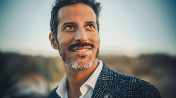 portrait en gros plan d’un homme adulte heureux avec moustache et barbe posant pour la caméra. bel homme de race blanche multiethnique d’âge moyen dans un costume charmant souriant. édition de couleurs chaudes. - charmingly photos et images de collection