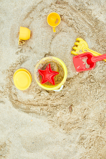 Top view, flat lay of scattered plastic beach toys on sand background, family summer vacation, Background with empty space for text