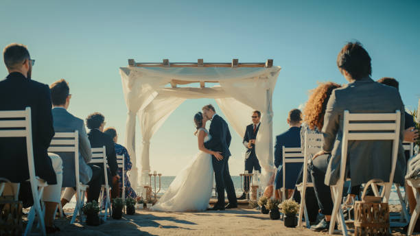 bella sposa e sposo durante una cerimonia di nozze all'aperto su una spiaggia oceanica. luogo perfetto per coppie romantiche per sposarsi, scambiare anelli, baciare e condividere celebrazioni con amici multietnici. - wedding beach bride groom foto e immagini stock