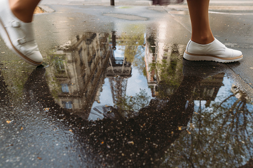 Close up photo of girl stepping over a puddle. In the puddle reflected Eiffel Tower. Woman wear stylish white boots. Travelling to Paris. Wanderlust.