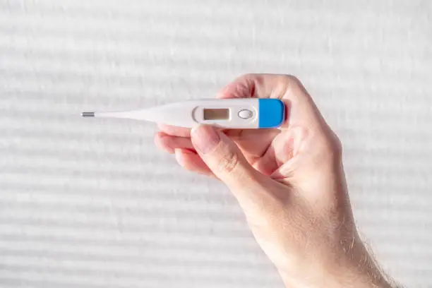 Person hold a Medical Thermometer on the White Wall Background closeup