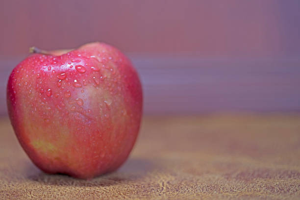 red apple in purple light on brown leather background and inspiration