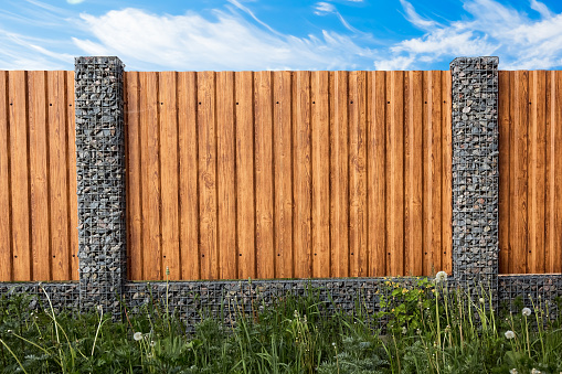 Gabion fence. Posts full of stones with sections from wooden planks. Countryside style. Exterior garden element design. Security wall. Natural materials. Isolated. Nature texture. Close-up.