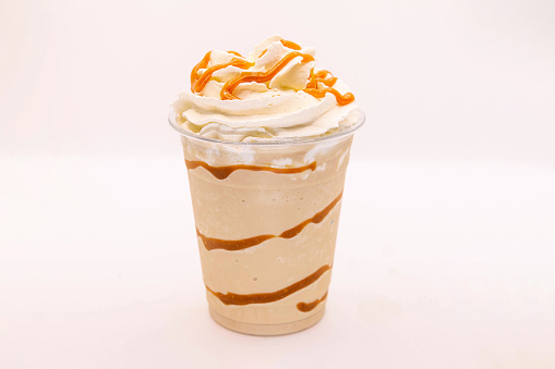 Caramel flavoured frappe served in a plastic cup with whipped cream and dressing.