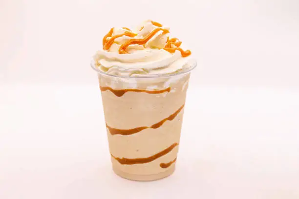 Photo of Caramel flavoured frappe served in a plastic cup with whipped cream and dressing.