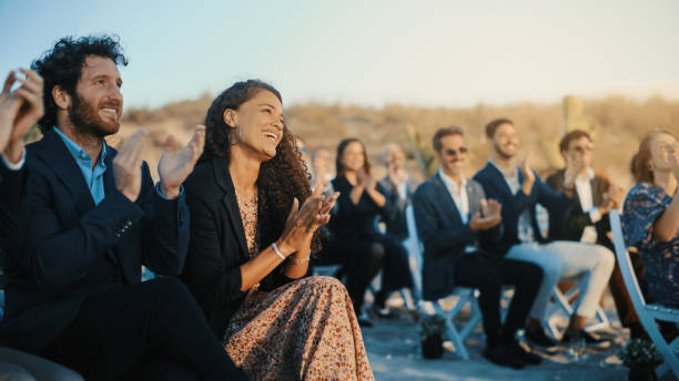 excited guests sitting in an outdoors venue and clapping hands. multiethnic beautiful diverse crowd celebrating an event, wedding or concert. inspiring day with beautiful warm weather. - wedding behavior horizontal men imagens e fotografias de stock