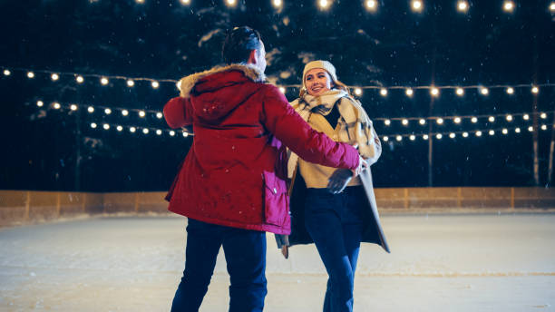 istock Romantic Winter Snowy Evening: Ice Skating Couple Having Fun, Step on Ice Rink and Start Dancing, waltzing. Pair Figure Skating. Tender Young People, Boyfriend and Girlfriend in Love. Wide Shot 1388579321
