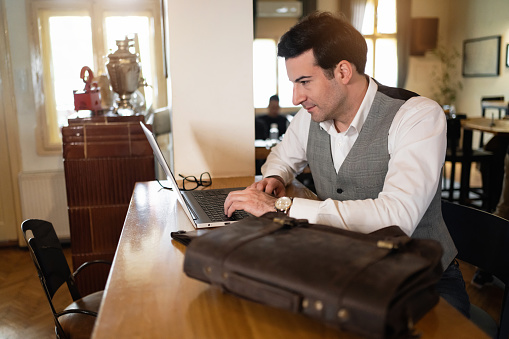 Modern Caucasian businessman working on laptop from modern coffee shop/restaurant