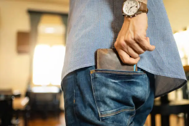 Unrecognizable Caucasian man puts his leather wallet into back pocket of the jeans