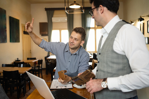 Caucasian man refuse to have his friend pay the bill at the coffee shop, gesturing to the waiter for the bill