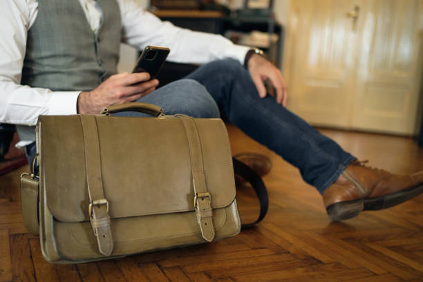 Side-view of unrecognizable businessman sitting on the floor and using mobile phone