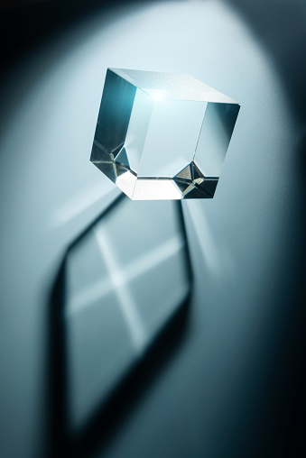 The glass cube casts a shadow on a blue background. Abstract composition with transparent prism and selective focus.
