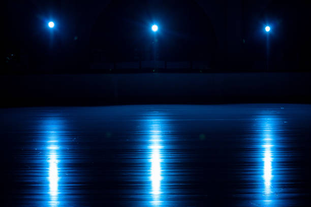 Smooth, shiny surface of an ice rink with reflected by spotlights. Dark empty ice arena with soft blue light. Concept of winter sports games, hockey, figure skating. Icy background of slippery ice, frosty space for training and performance. Close up.