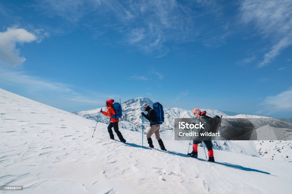 Successful mountain climber team is climbing in a row on the ridge of the  high altitude snowy mountain summit in winter Alpinist climbers are walking on snow mountain crest on extreme harsh conditions before reaching the peak Mountain Stock Photo