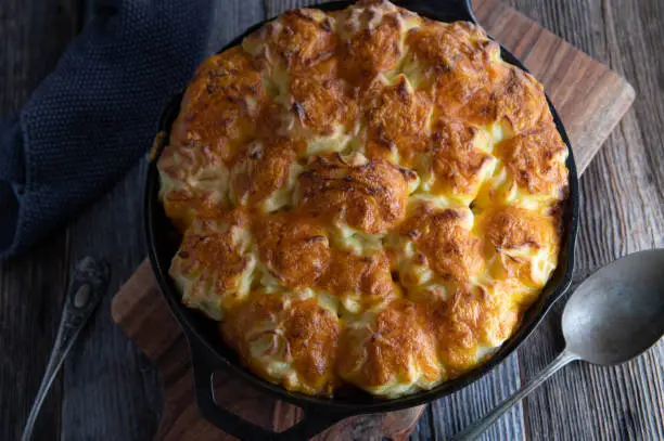 Traditional irish savory shepherd´s pie with potato cheddar cheese topping. Served in a rustic cast iron pan on dark wooden table background. Closeup and overhead view