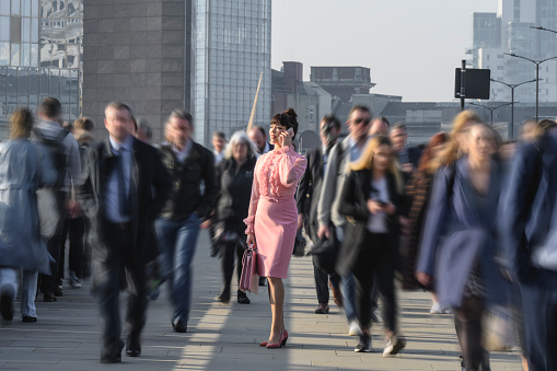 Three-quarter front view of smiling businesswoman with briefcase stopped on London Bridge while walking with crowd from Southwark to financial district.