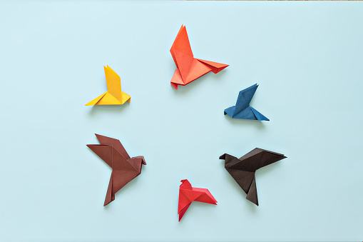 six paper origami pigeons different colors arranged in circle on light blue background, copy space