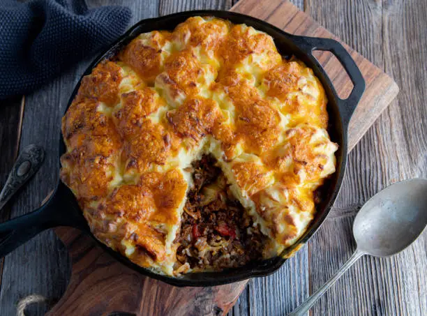 Delicious savory pie, shepherd style. Cooked with minced meat and cabbage. Oven baked with a delicious mashed potato, cheese crust. Served in a rustic cast iron skillet on wooden table. Overhead view.
