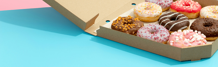 Set of yummy colorful donuts in paper box on blue background. Online delivery take away food. Mock up template for bakery