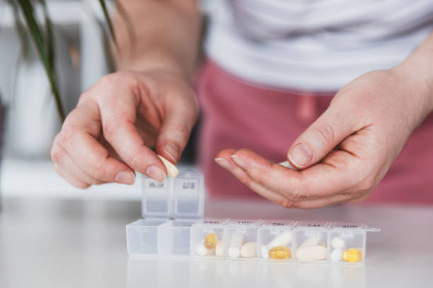 Medical pill box with tablet doses for daily take medicine with drugs, capsules Female hands sorting pills. Young woman getting her daily vitamins at home. Closeup of medical pill box with doses of tablets for daily take a medicine with different white, yellow drugs and capsules change dispenser stock pictures, royalty-free photos & images