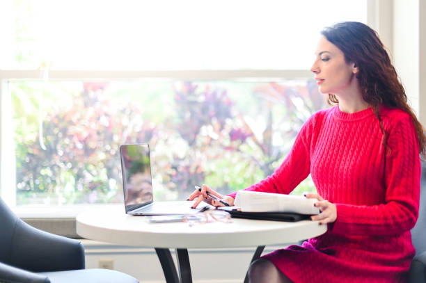 istock Woman using a laptop at a small table at home or remote location, working or studying 1388600580