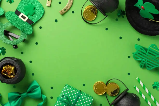 Photo of Top view photo of party glasses leprechaun hat straws green bow-tie giftbox horseshoe shamrocks confetti and pots with gold coins on isolated pastel green background with blank space in the middle